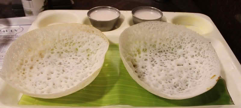 Two Appam pancakes served with coconut milk arranged neatly on a tray