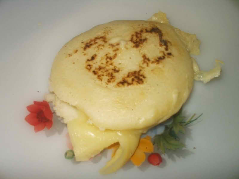 A plate featuring a golden arepa, a traditional cornmeal dish, with a cheese filling, garnished and ready to be enjoyed