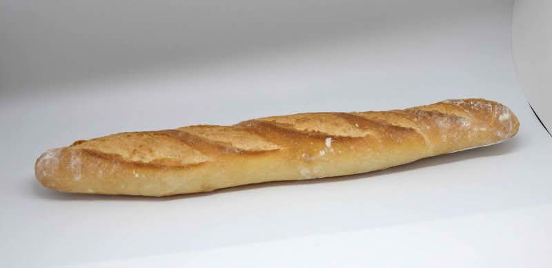 A baguette resting on a white surface, showcasing its long shape and crusty exterior