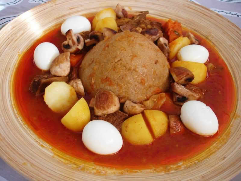 A plate of Bazin (center) served with a stew and whole hard-boiled eggs