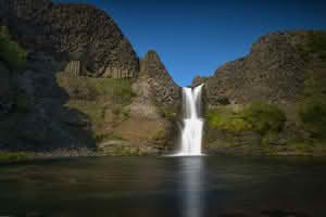A stunning view of the Selfoss Waterfall cascading into a river, surrounded by natural beauty and rugged terrain