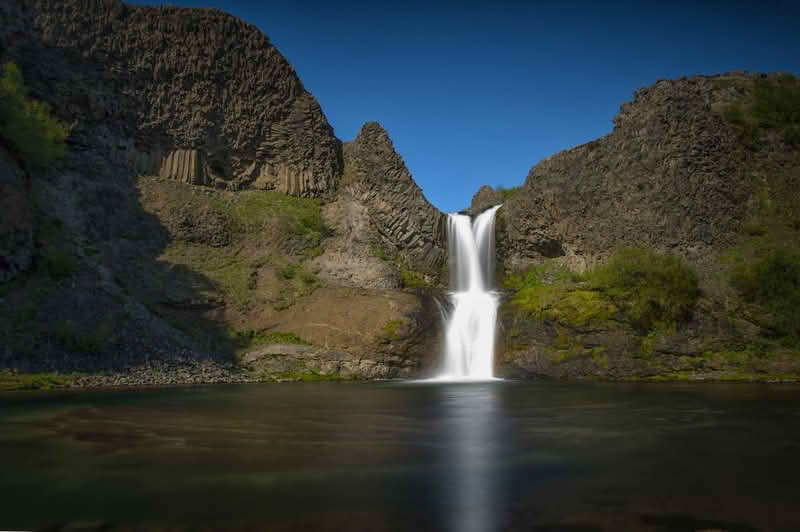 A stunning view of the Selfoss Waterfall cascading into a river, surrounded by natural beauty and rugged terrain