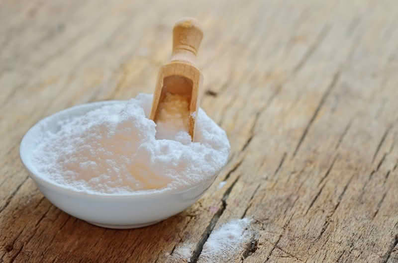A bowl of baking soda with a wooden spoon resting on top, ready for use in baking or cooking