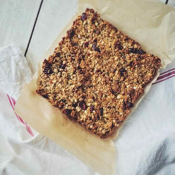 High-angle close-up view of a rectangular granola bar resting on a sheet of brown parchment paper, which is itself laid over a white linen cloth with thin red stripes