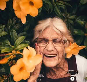 Roberta Johnson smiling with eyes closed near a plant with orange flowers